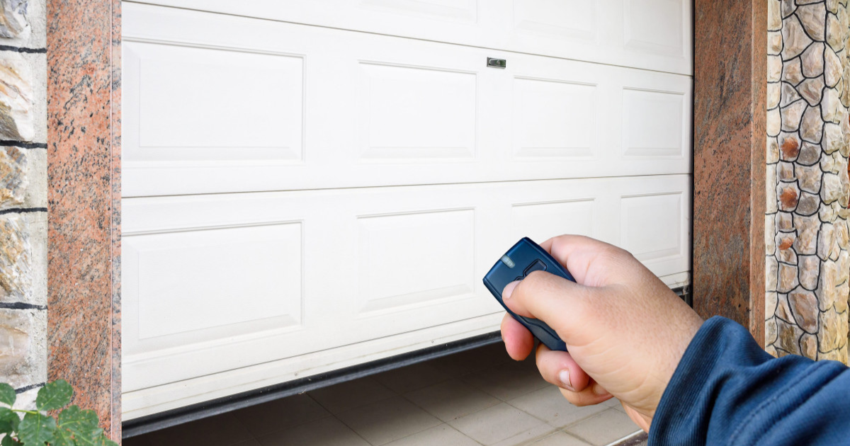 Person using a remote control to operate a white garage door.