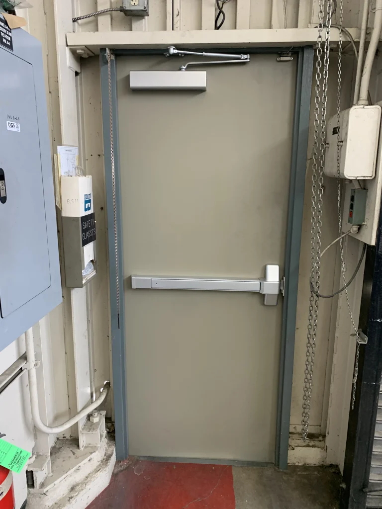 A durable beige commercial hollow metal door with a crash bar and door closer, illustrating how proper hardware choices can maximize hollow metal door lifespan.