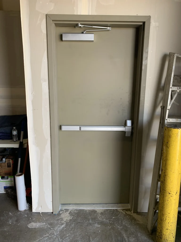 A commercial beige hollow metal door equipped with a panic bar and door closer, highlighting solutions for hollow metal door problems in Sacramento